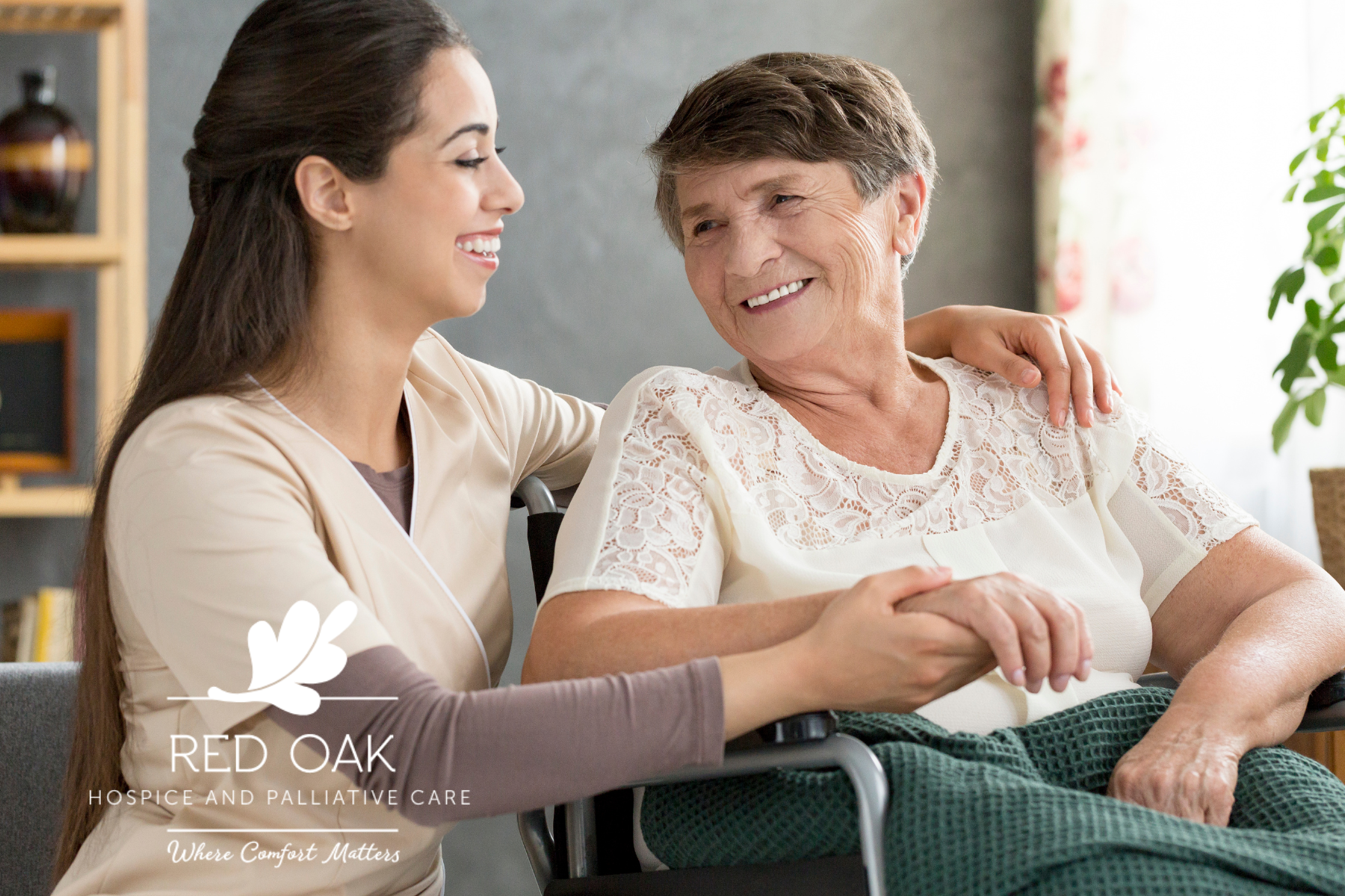 Caregiver smiling and holding the hand of a senior woman in a wheelchair during hospice care.