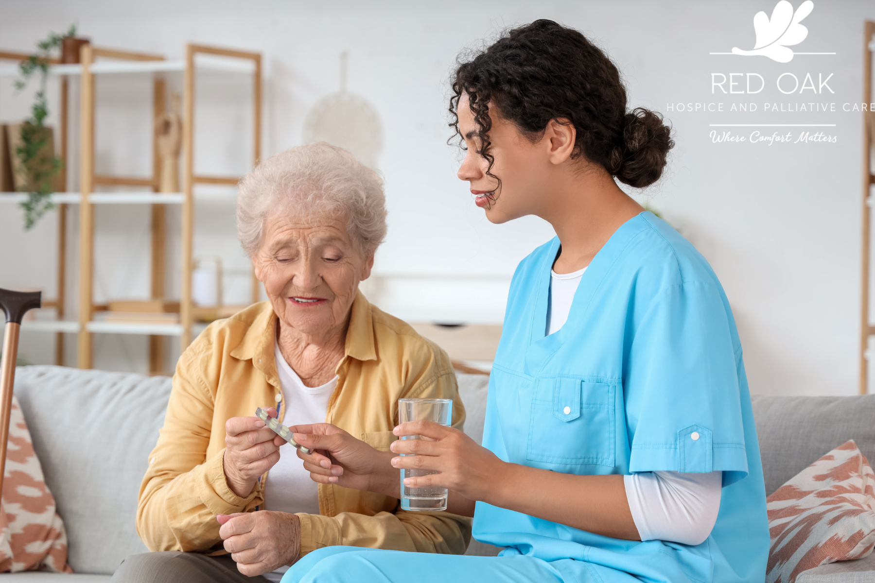 A nurse in blue scrubs assists an elderly woman with medication and a glass of water at Red Oak Hospice and Palliative Care.
